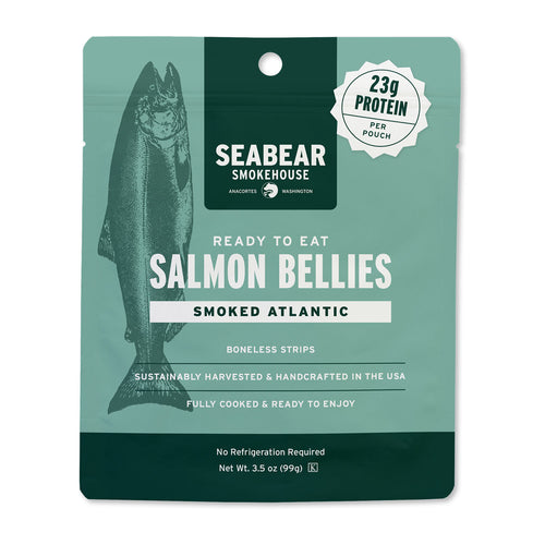 A package of Seabear Smokehouse Salmon Bellies, Smoked Atlantic flavor. The packaging is a resealable pouch with a sage green and dark green design, featuring a graphic of a salmon and white text detailing the product's protein content and features.