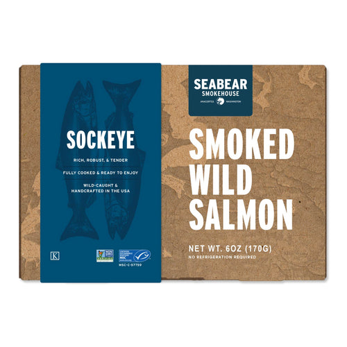 A package of Seabear Smokehouse Smoked Wild Salmon, featuring a split design with a dark blue left panel showing fish silhouettes and white text, and a brown kraft-paper right panel with large white text.