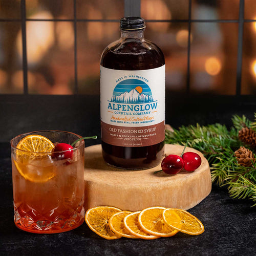 Alpenglow cocktail syrup bottle with a glass of cocktail and garnishes on a wooden board. | Alpenglow Old Fashioned Cocktail Syrup | Made In Washington | Local Gifts for Bartenders