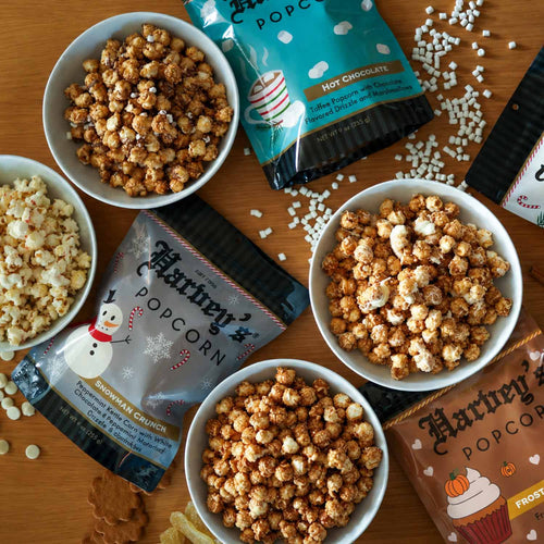 Four bags of Harvey's Popcorn in Sugar & Spice, Frosted Pumpkin, Snowman Crunch, and Hot Chocolate on a white background.