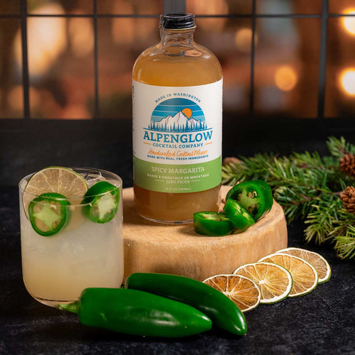 Alpenglow cocktail bottle with a drink and garnishes on a wooden board. | Alpenglow Cocktail Co. Spicy Margarita Mixer | Made In Washington  | Home Bartending Favorite