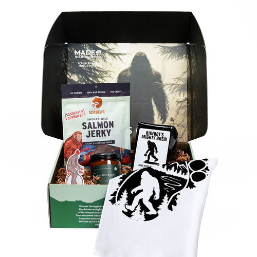 Box of themed products including salmon jerky and Bigfoot-themed items. | Made In Washington | Sasquatch Gift box with salmon jerky, candle, and other bigfoot items on a white background | Shop Local Gifts