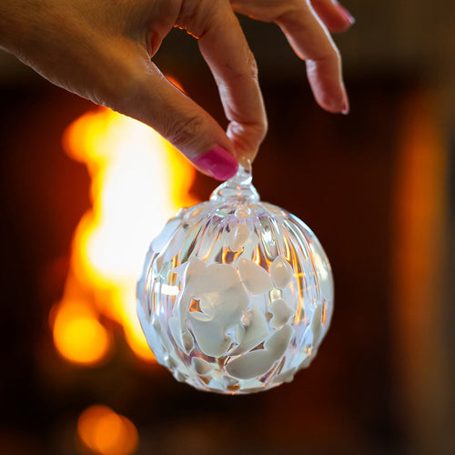 Hand holding a decorative glass ball with a floral design against a warm, blurred background. | 2025 Limited Edition Christmas Ornament | Made In Washington