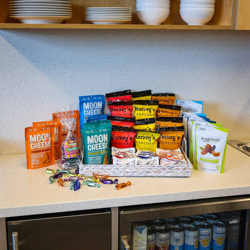 Assorted snack packages on a kitchen counter with shelves in the background | Made In Washington | Grab & Go Snacks for the the team | Shop Local Office Gifts
