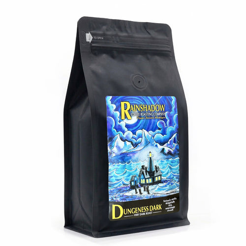 Dungeness Very Dark black coffee bag with a colorful label featuring a lighthouse and mountain scene, on a white background.
