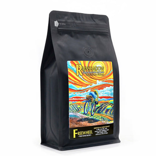 Freewheel Two Tone Blend black coffee bag with colorful 'Rainshadow' label featuring a cyclist on a mountain bike.