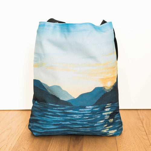 Amy Duffy Tote bag with a scenic design of mountains and sky on a wooden floor.