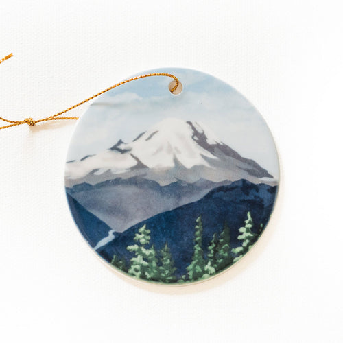 The Mountain Is Out round ceramic ornament with mountain and forest design on a white background