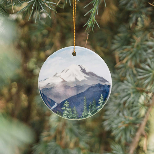 The Mountain Is Out round ceramic ornament with mountain and forest design on a white background