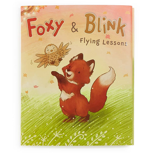 Children's book cover titled 'Foxy & Blink Flying Lessons' featuring an illustration of a fox flying a small bird, set against a warm peach sky and green grass background.