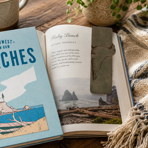 A rectangular dark grey bookmark featuring a raised relief carving of a harbor seal, shown against a solid white background.