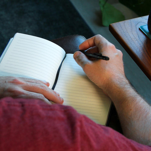 A topaz faux-leather notebook featuring a black silhouette of the Seattle skyline, including the Space Needle and Mount Rainier, with the word 'Seattle' written in black script near the bottom right.