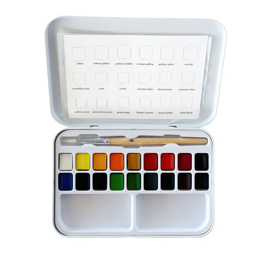 An Emily Lex Studio watercolor paint set in a white metal tin, shown open with 18 color pans, a wooden-handled brush, and a color chart sheet inside the lid on a white background.
