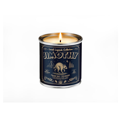 A tin candle from the Local Legends Collection called JIMOTHY, featuring a dark navy blue label with gold vintage-style text and illustrations of a racoon, trees, and a moon, set against a plain white background.