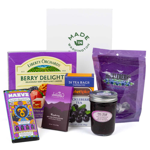 A curated berry-themed gift basket featuring a box of Liberty Orchards Berry Delight, a bag of Huckleberry Candy, a jar of Marionberry Jam , a box of Dolcetta Raspberry Chocolate bar, and a colorful Maeve Hungry Blackberry chocolate bar, arranged in front of a white 'Made Washington' box on a white background.