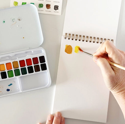 A white spiral-bound watercolor paper pad with a small paint palette and paintbrush illustration on the cover, labeled 'watercolor paper' and '12 sheets | 120 lb | 5 x 7 inches'.