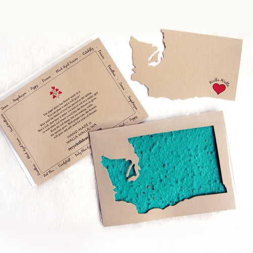 A plantable seed card featuring a turquoise blue textured shape resembling the state of Washington, beneath a cut out of the state in a light tan background.