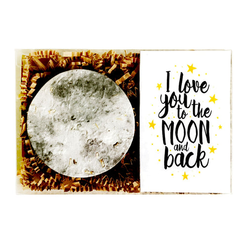 A plantable gift card featuring a large textured moon embedded with seeds on brown crinkle paper beside the phrase 'I love you to the MOON and back' in black script with small yellow stars on a white background.