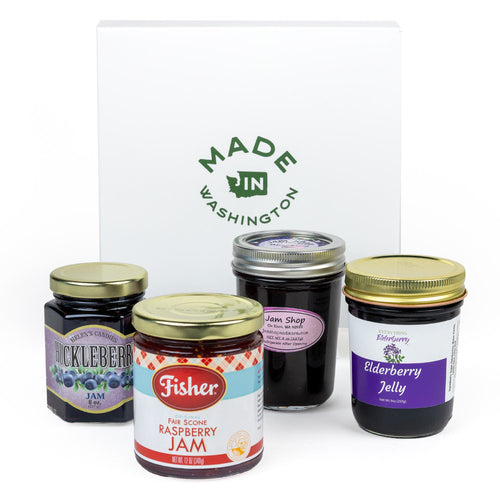 A gift set of four berry preserves jars arranged in front of a white box printed with the green 'Made in Washington' logo. The jars include Hucklleberry Jam, Fisher Family Scone Raspberry Jam, Jam Shop Marionberry Jam, and Elderberry Jelly.