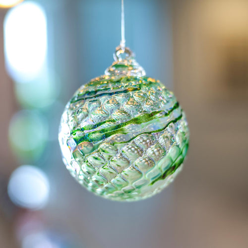 A textured green and iridescent glass Christmas ornament hanging from a thin string against a softly blurred bokeh background.