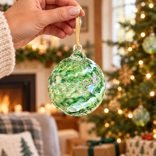 A textured green and iridescent glass Christmas ornament hanging from a thin string against a softly blurred bokeh background.
