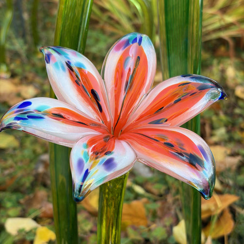 Low angle view of an orange speckled hand-blown glass lily flower on a green stem.