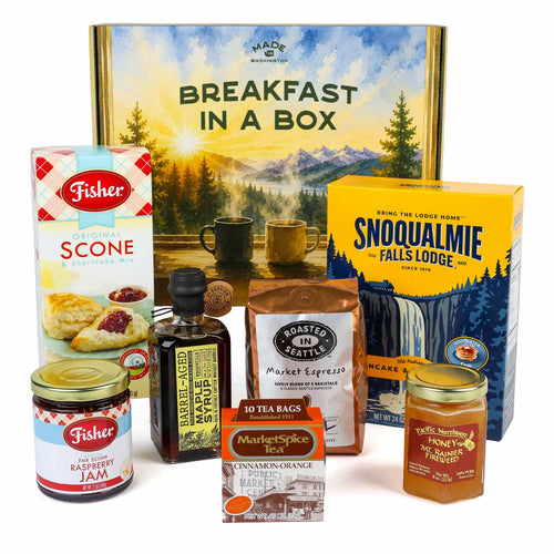 Assorted food and beverage products including scones, maple syrup, coffee, jam, and tea on a white background in front of a box designed with a watercolor-like Pacific Northwest forest and mountain scene and the words Breakfast In A Box.