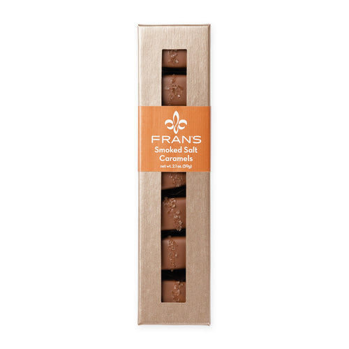 A tall, narrow box of Frans Smoked Salt Caramels on a plain white background. The packaging is a light tan cardboard style with a central orange band featuring the white Frans logo and text, and vertical windows showing the chocolate caramels inside.