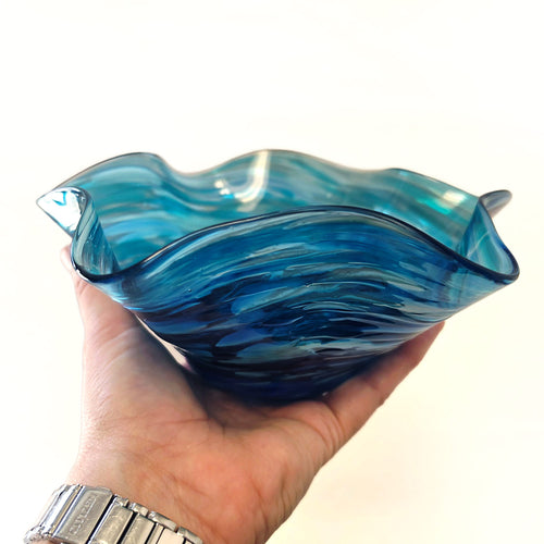 A sculptural glass bowl with a wavy, flared rim and a matching textured glass base, shown on a clean white background with a soft reflection underneath.