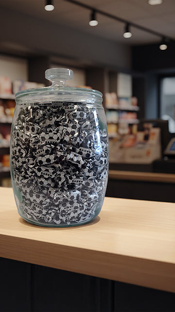 Jar filled with small black and white soccer bonbons on a wooden surface in a store setting.
