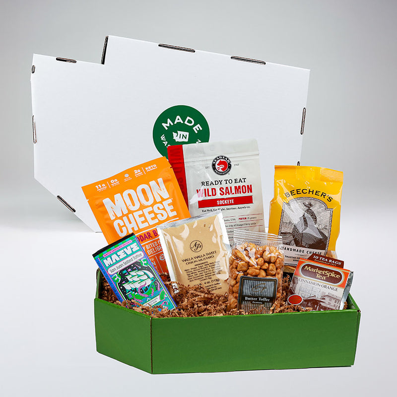 Assorted snacks and treats in a green and white Washington shaped box with visible brand names on a gray background | Made In Washington Gift Baskets | Ready-to-give baskets, no wrapping required | Explore ready-to-gift baskets for Chistmas