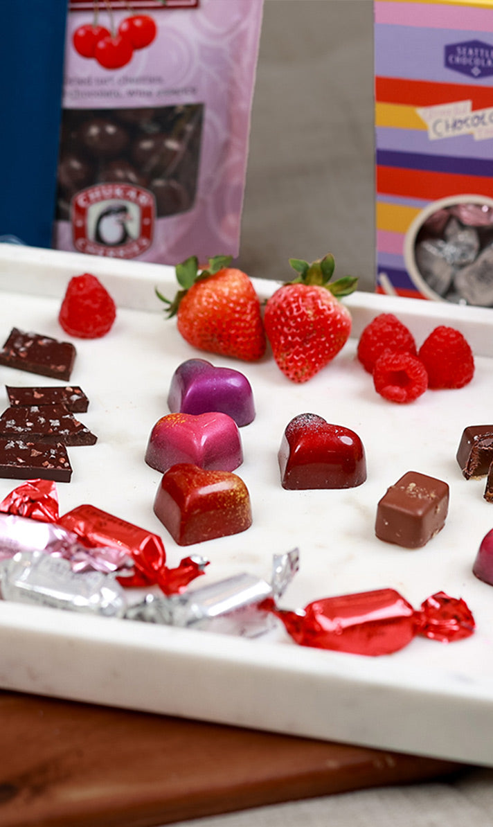 Assorted chocolates and berries on a white plate with chocolate packaging in the background. | The best local Valentine's Day gifts from Washington State | Made In Washington Gift Stores