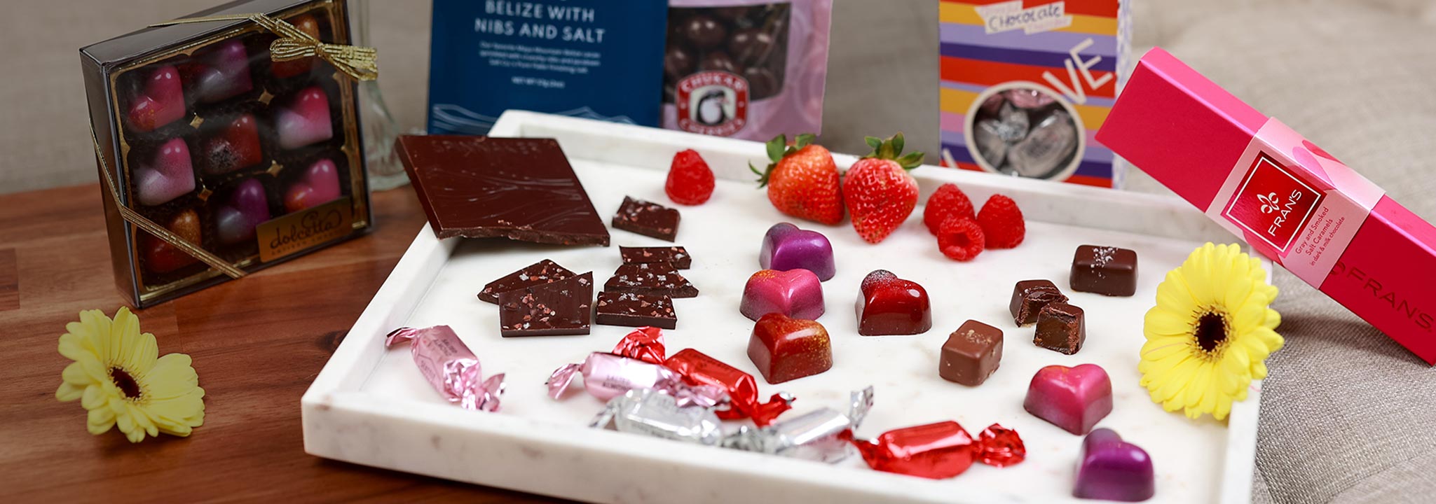Assorted chocolates on a white tray with flowers and a box of chocolates in the background. | Shop for local Valentine's Gifts from Made In Washington Gift Stores